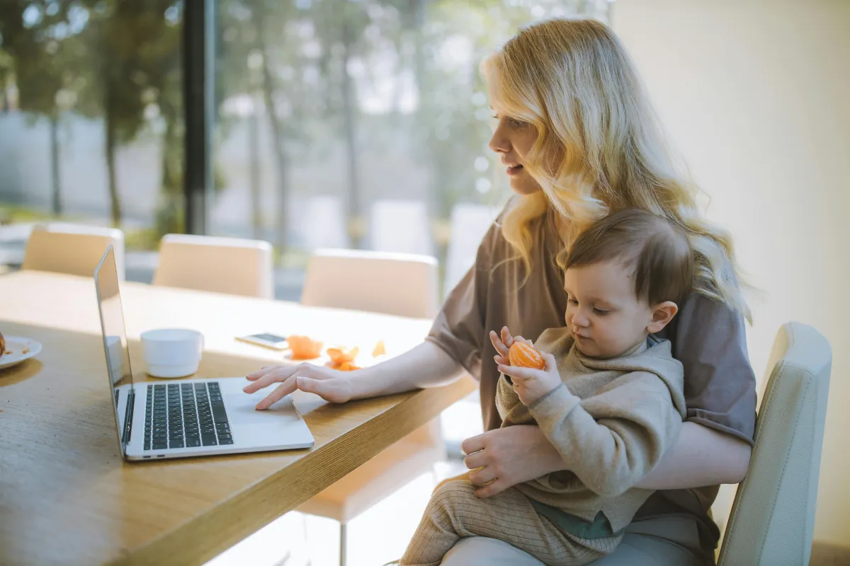 Woman working from home on a laptop with a toddler in her lap