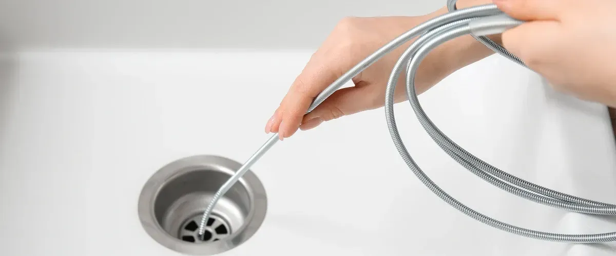 Using a metal drain snake to remove blockage from a sink drain