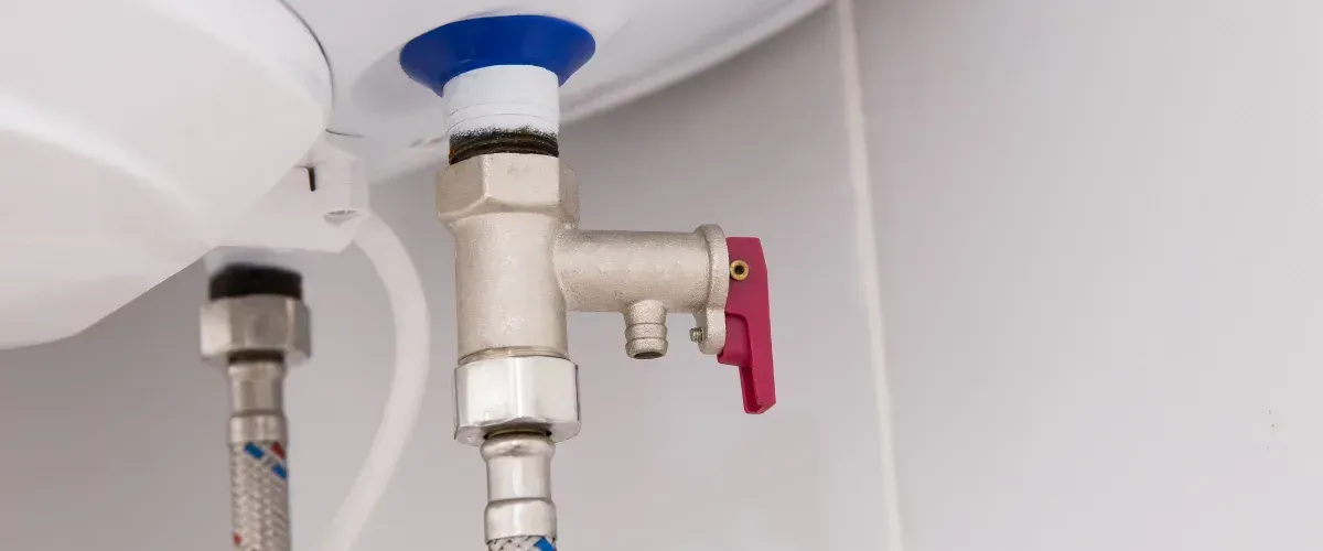 Close-up of a water heater with a silver valve, braided hose, and a red lever handle against a white background.