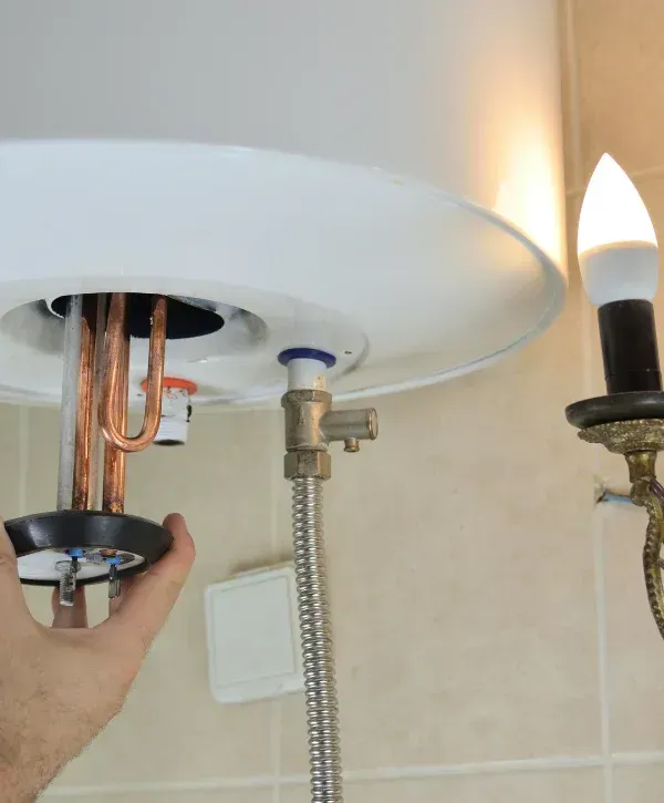 A person's hand installing the heating element into a white electric water heater, showing internal copper coils.