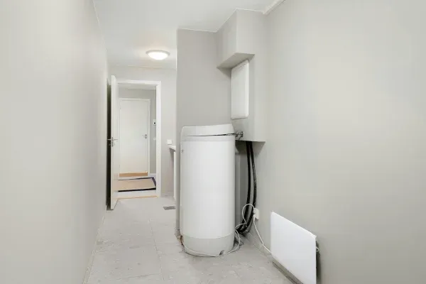 A narrow hallway leading to a partially open white door, featuring a white water softener and water heater.