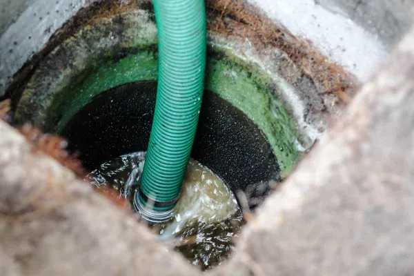 A close-up view looking down into a pit with a green hose pumping dirty, murky water.