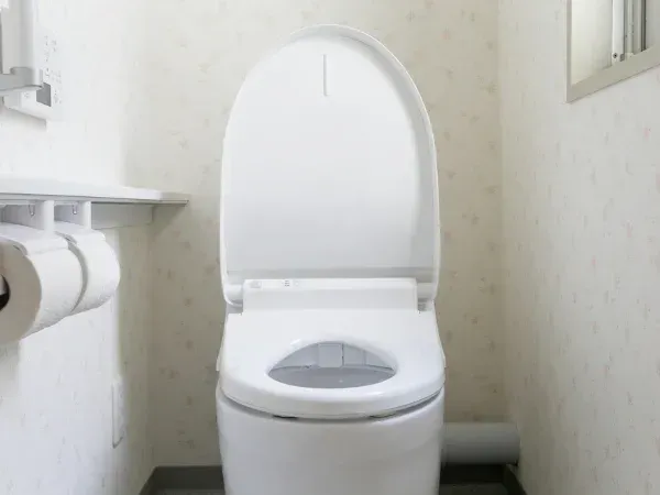 A clean white modern toilet with an open lid and smart features, set against floral wallpaper in a bright bathroom.