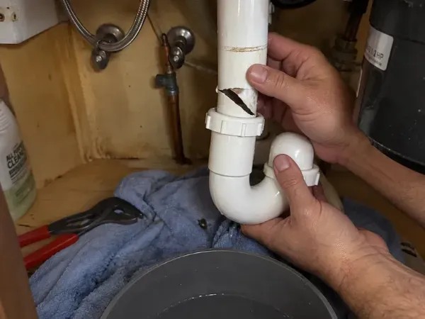 Plumber repairing a leaking sink pipe under a bathroom sink