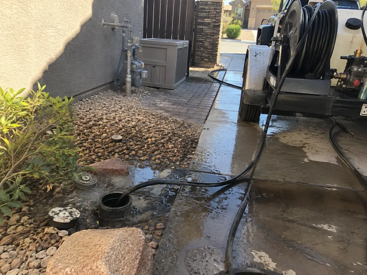 A utility trailer with a hose reel connected to a ground drain, surrounded by wet concrete and gravel.