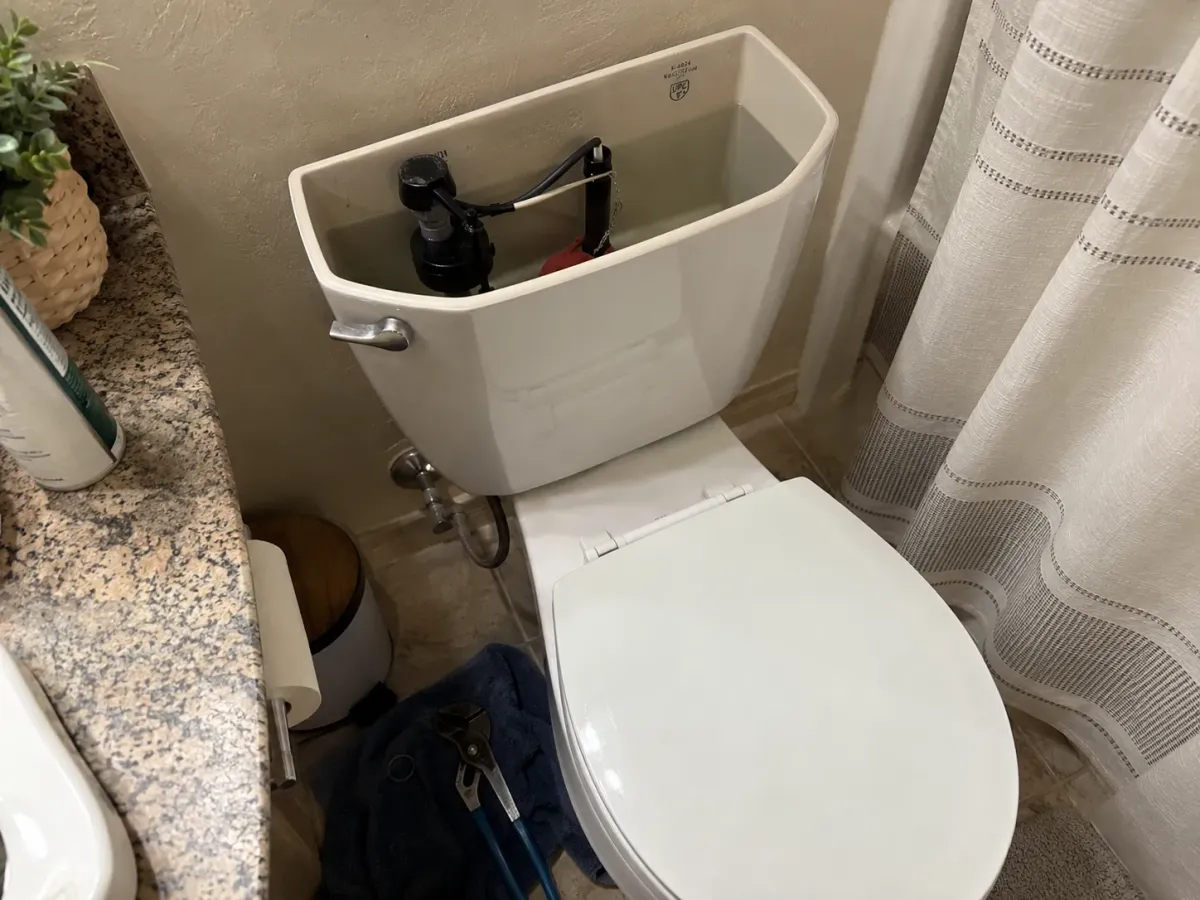 A top-down view of a white toilet with the tank lid removed, showing internal mechanisms and water.