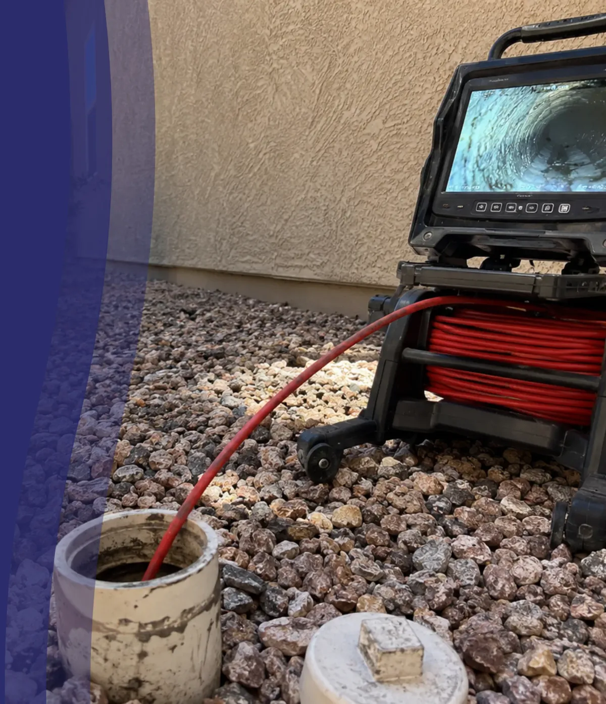 An outdoor drain pipe camera inspection setup with a red cable entering a white pipe and a monitor displaying the pipe's interior.