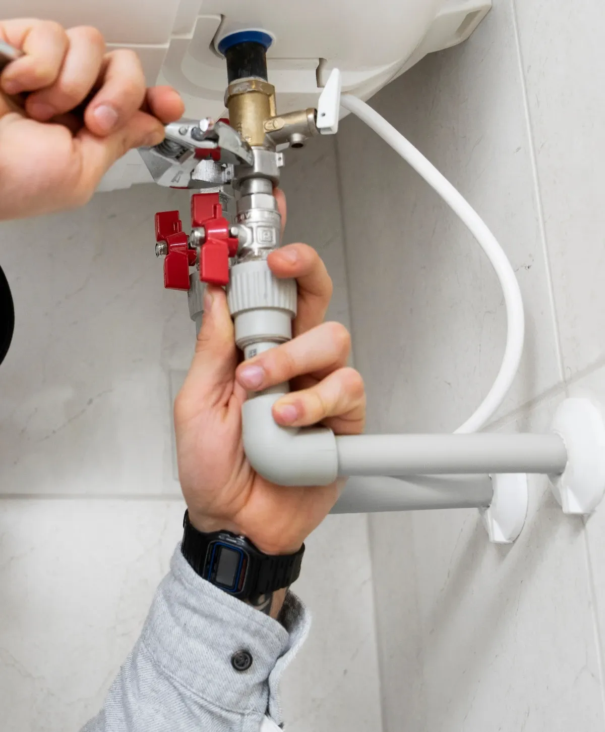 Close-up of a plumber's hands connecting plumbing pipes and valves to a water heater unit.
