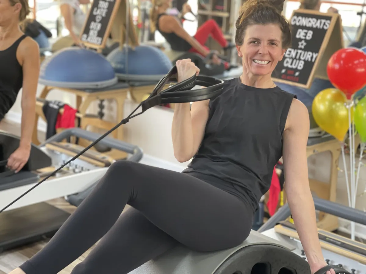 Happy Core10 Pilates member smiling while working out on the reformer, showcasing strength, confidence, and the benefits of Pilates fitness