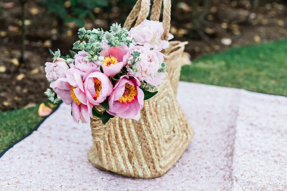 A basket of pink peonies on a picnic blanket in the park