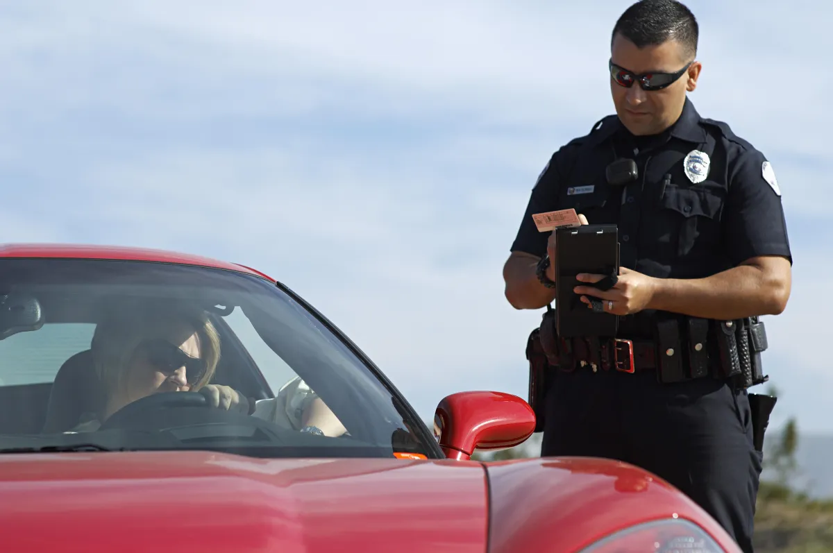 A police officer handing out a traffic ticket to a lady driving a red car