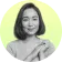 A person with short hair smiling at the camera, hands clasped. The background is light yellow-green.