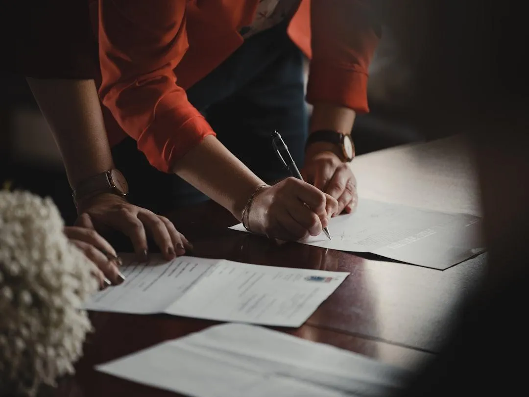 A professional team of three immigration consultants, two women and one man, seated at a round table in a bright office, reviewing documents together. The consultants are of different ethnic backgrounds, dressed in smart business attire, and appear focused and collaborative. Clean, modern photographic style.