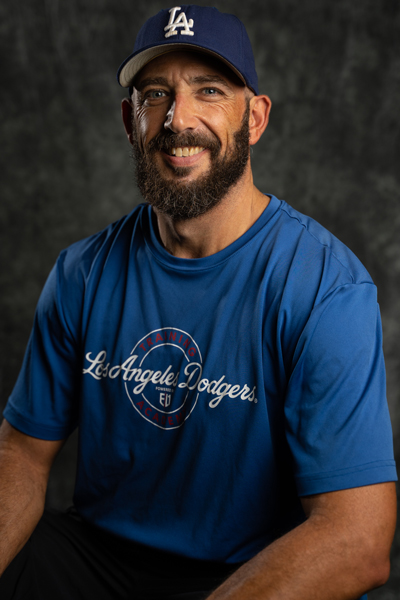 Photo of pitching coach smiling on a baseball field holding a baseball and glove
