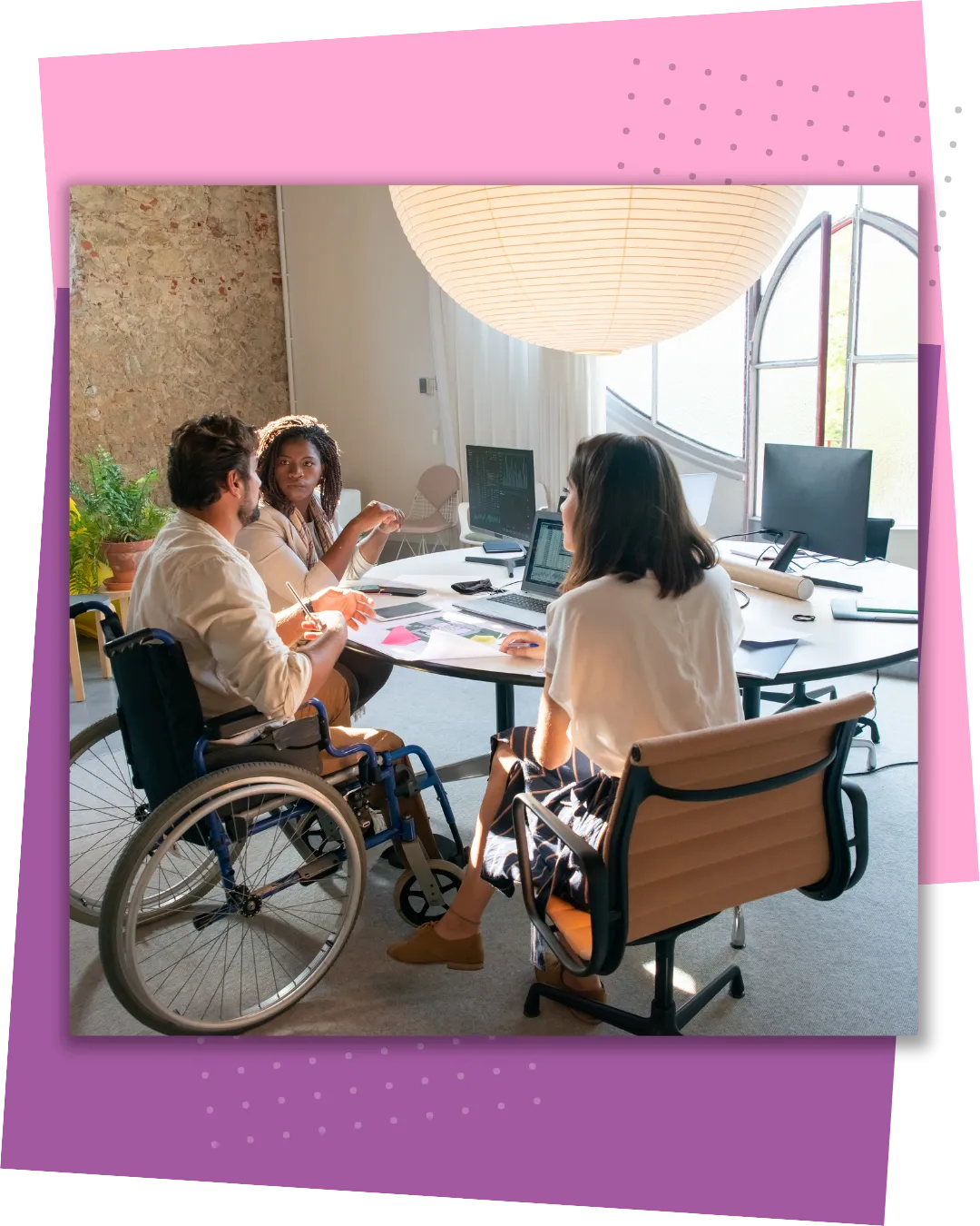 Three people sitting around an overall table having a business meeting. One of the three people is in a wheelchair.