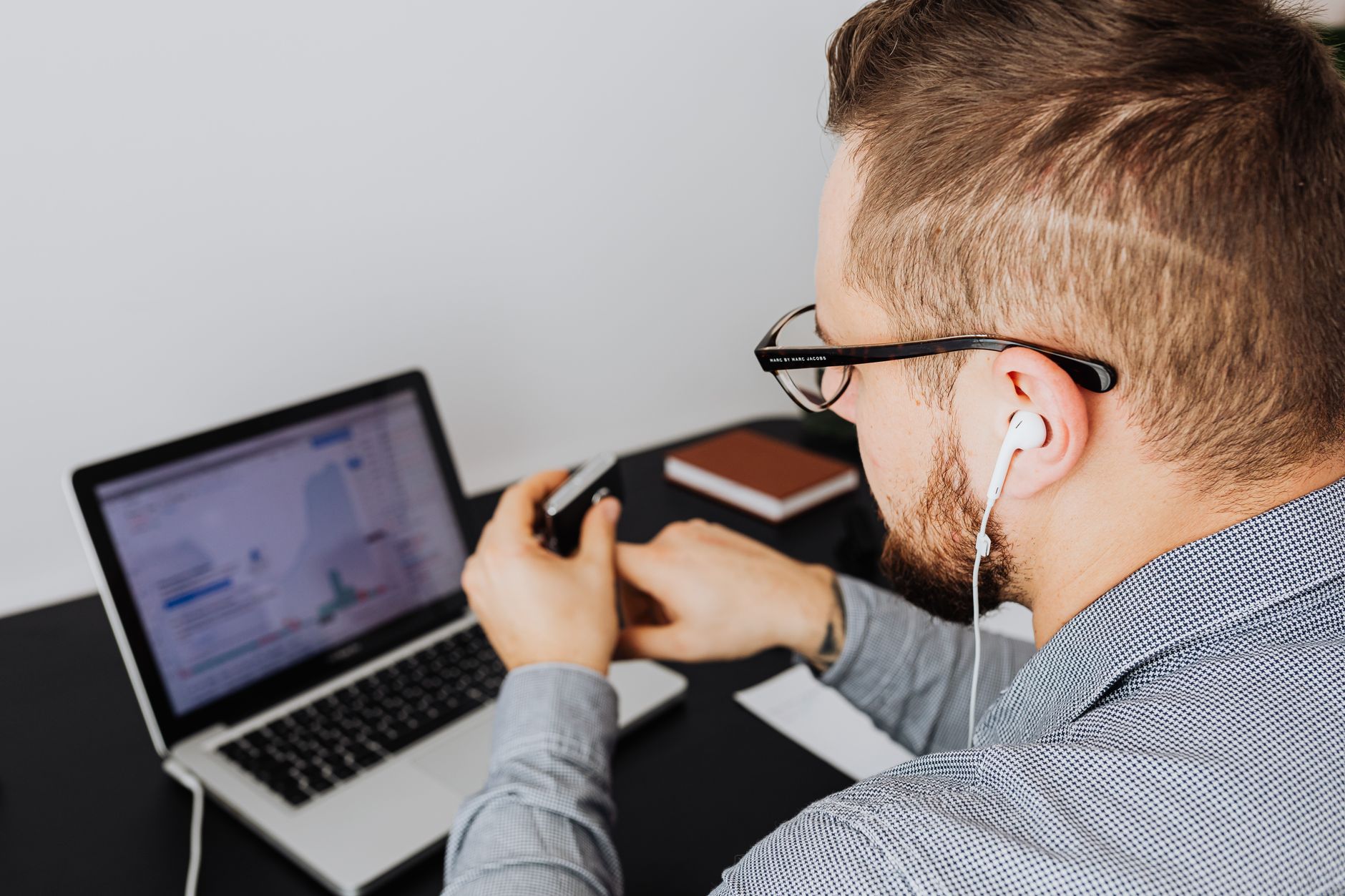 A business professional uses a laptop with charts and graphs while wearing earphones in an office setting.
