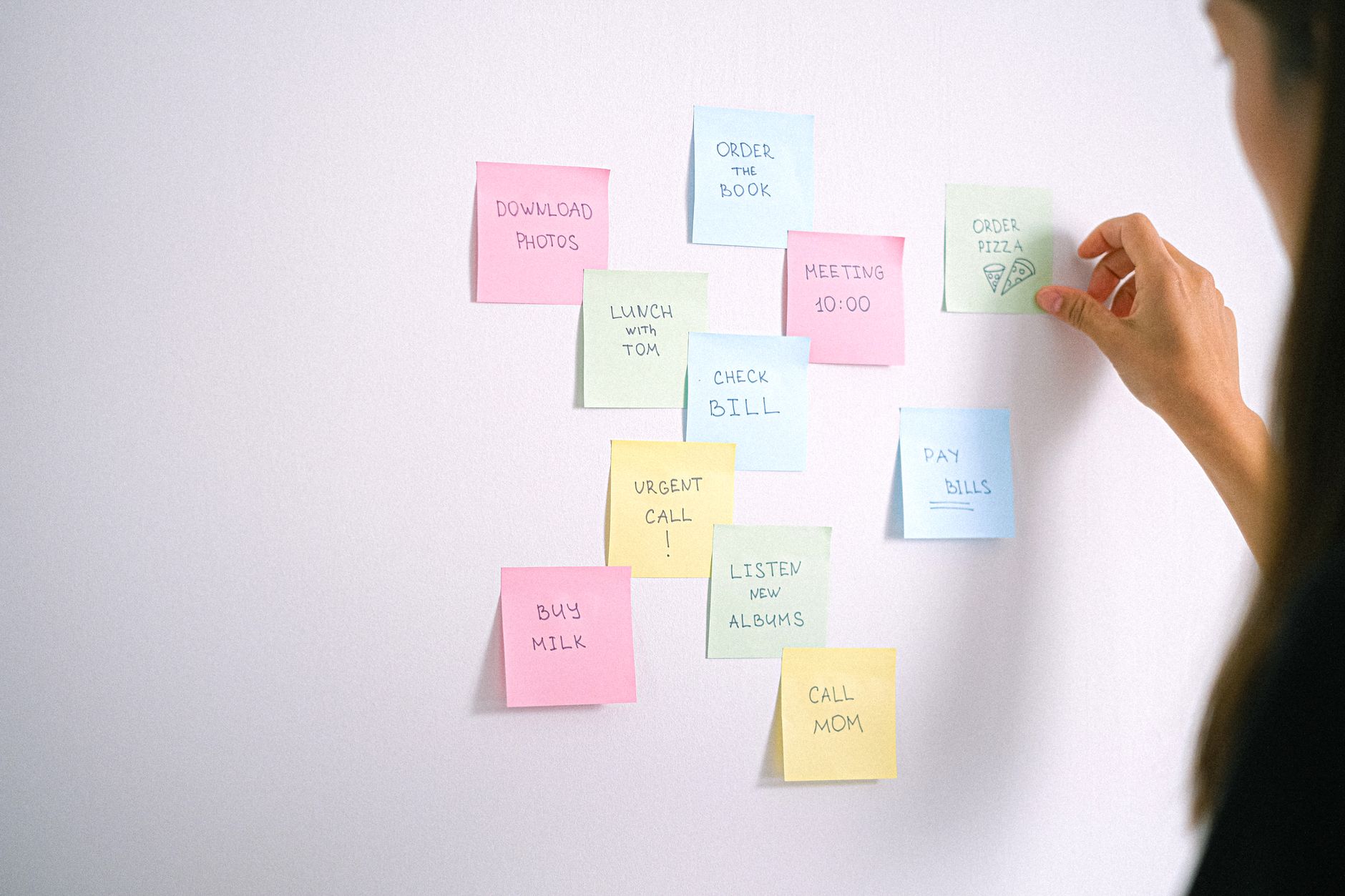 A collection of colorful sticky notes on a white wall with a hand organizing them.