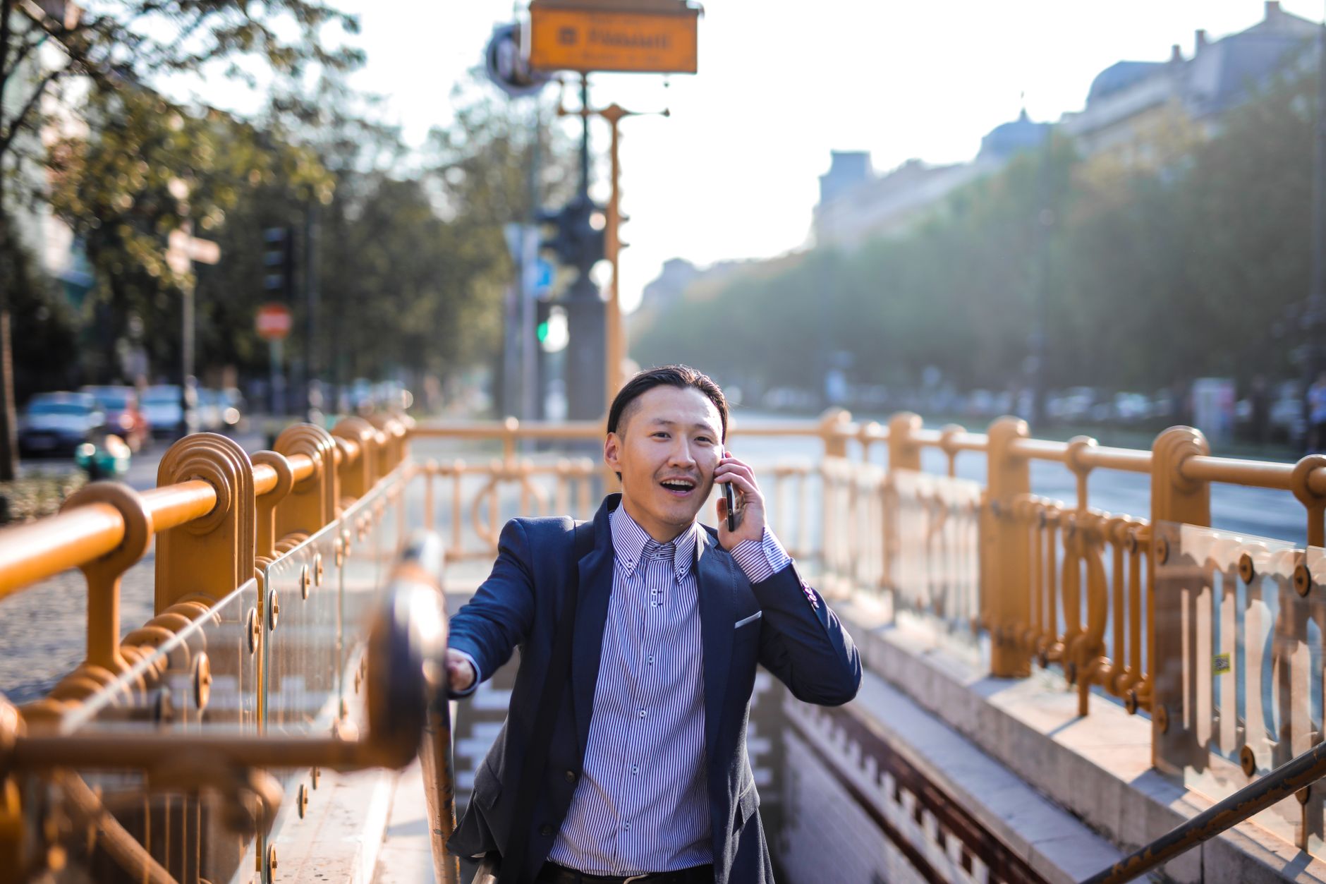 Asian businessman in casual wear talking on phone near an urban subway entrance.