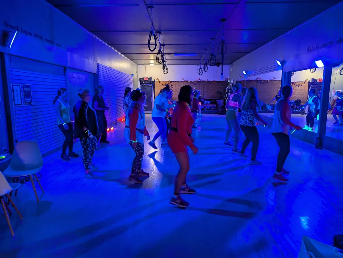 Smiling young woman mid-dance with neon rim lighting, waist-up, candid portrait