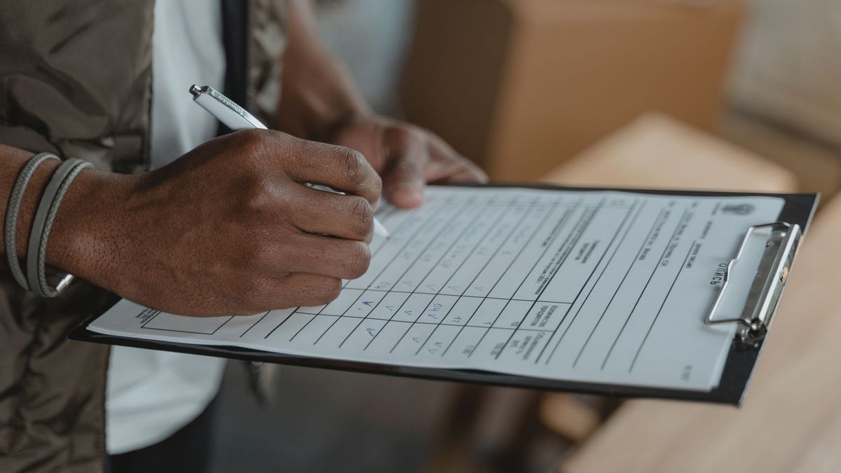 A hand fills in an export document on a clipboard beside packed cartons — paperwork prepared for every Ugandan fresh-produce shipment.