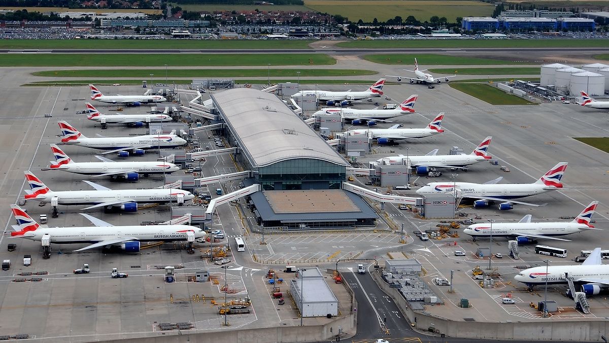 Aerial view of a London airport terminal with rows of aircraft at their stands — the scheduled-flight capacity that carries Ugandan produce to the UK.