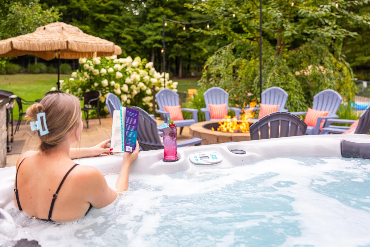 Guest relaxing in a 10-person hot tub with backyard views at Swimming in the Sunset, luxury Fennville MI vacation rental near Lake Michigan with pool and fire pit