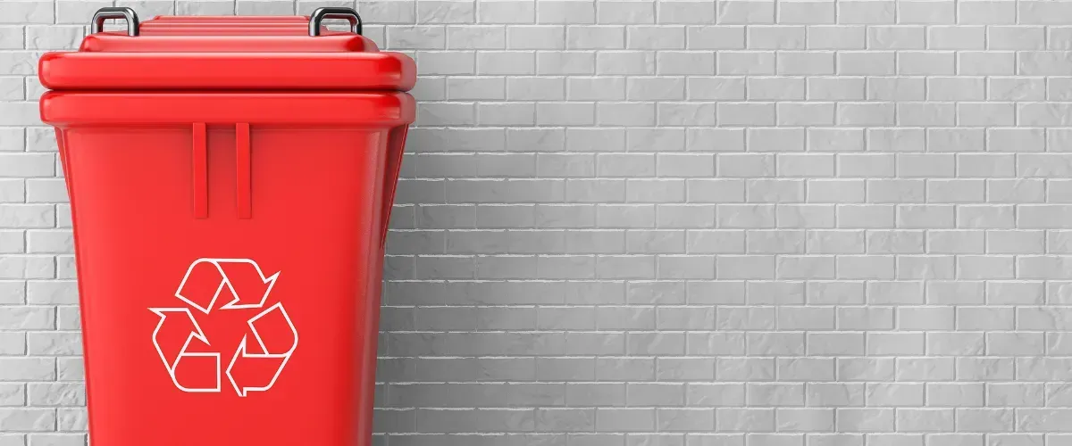 Red recycling bin placed in front of a light gray brick wall