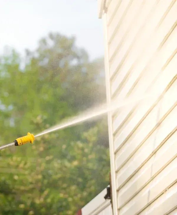 Pressure washing house siding to remove dirt and mildew.