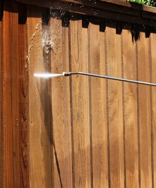 Close-up of power washing spray cleaning a wooden fence surface.