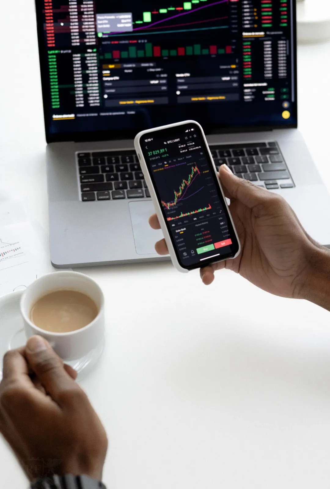 Mano sosteniendo un smartphone con gráficas financieras frente a una laptop con análisis de datos, simbolizando estrategia y crecimiento empresarial