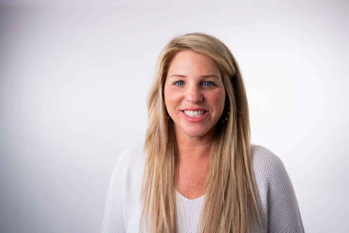 Kelly Brewin smiling in a professional headshot wearing a white sweater on a neutral background