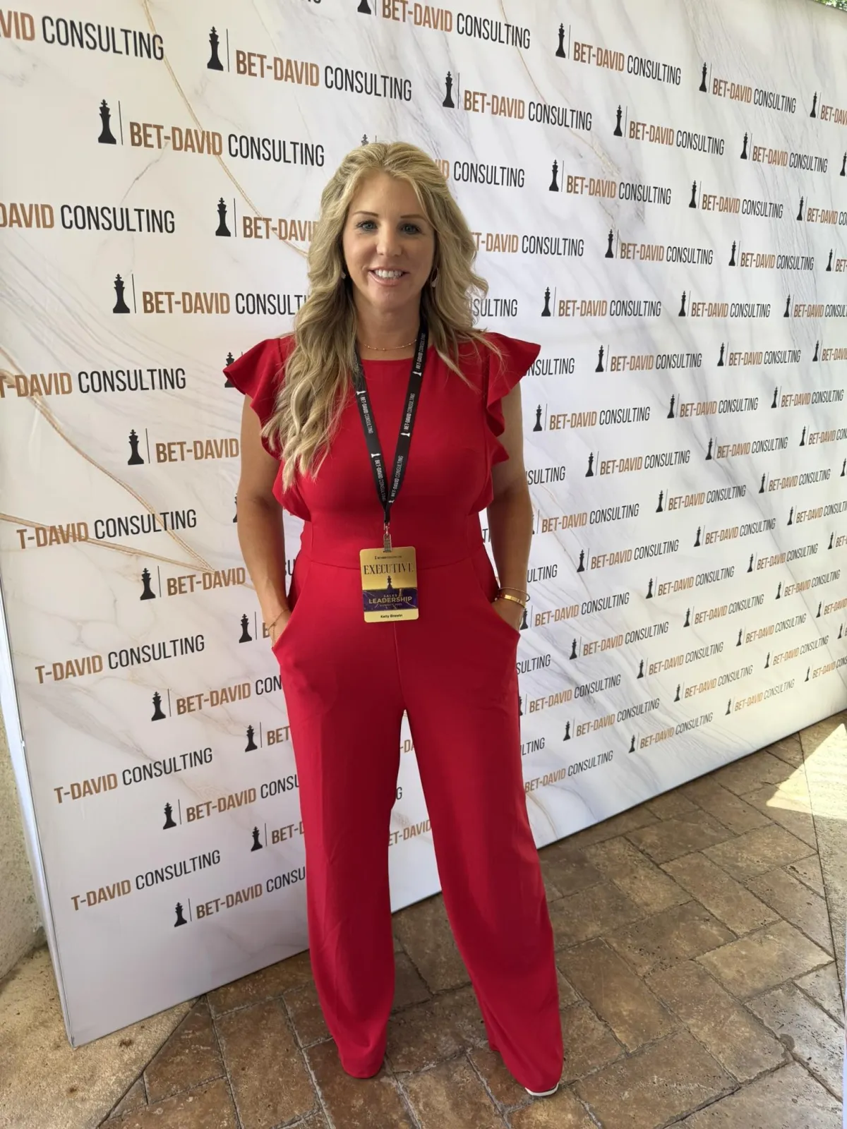 Kelly Brewin, entrepreneur, roofing specialist, and real estate agent in Jacksonville FL, standing in front of Bet-David Consulting step-and-repeat backdrop