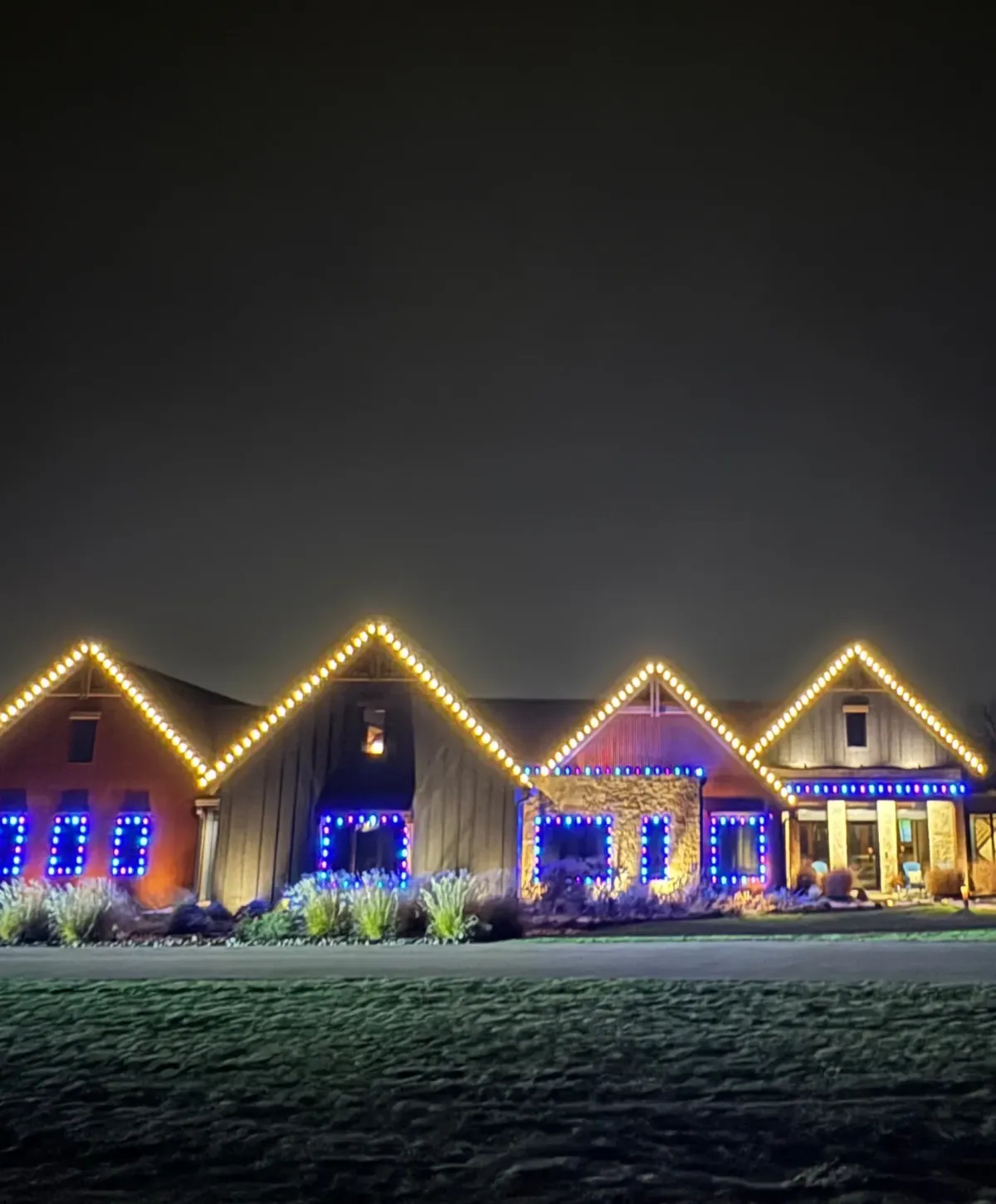 Front view of a large home decorated with vibrant Christmas and holiday lights at night