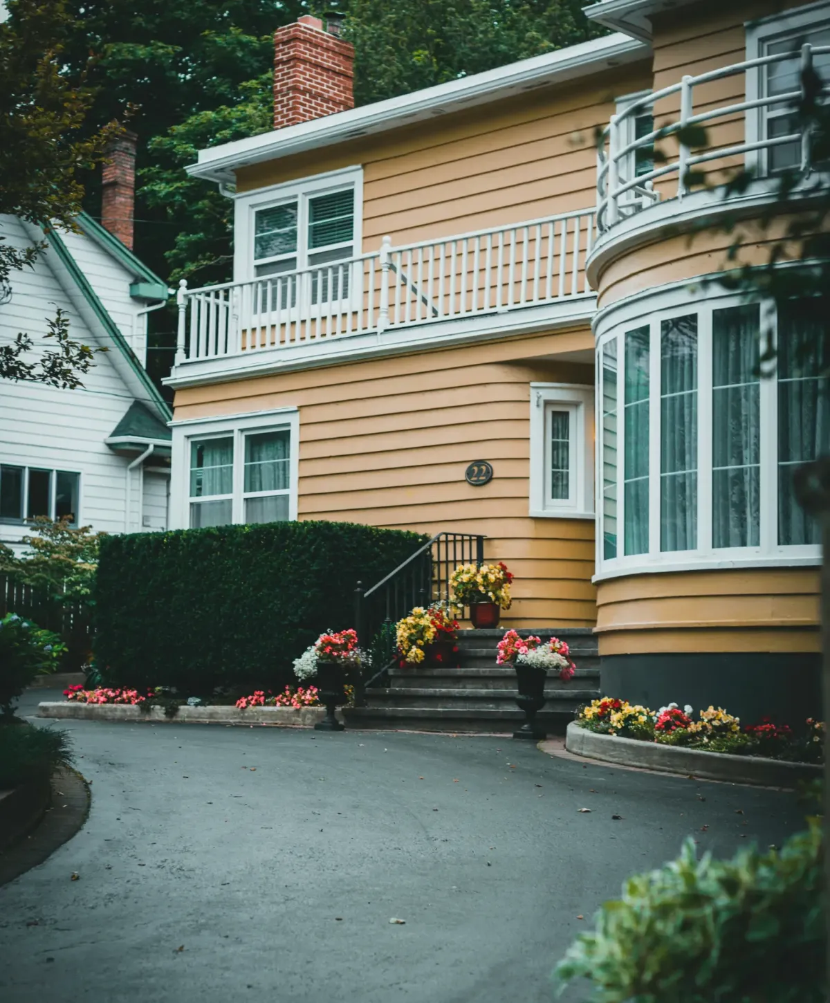  A quaint yellow house with flowerpots and a clean driveway, exuding charm and curb appeal