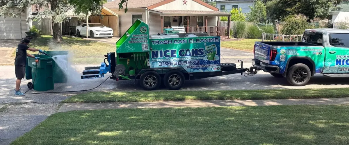Worker pressure washing trash bins using a mobile trash can cleaning trailer parked in a neighborhood