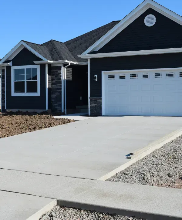 Freshly poured concrete driveway in front of a dark modern ranch-style home.