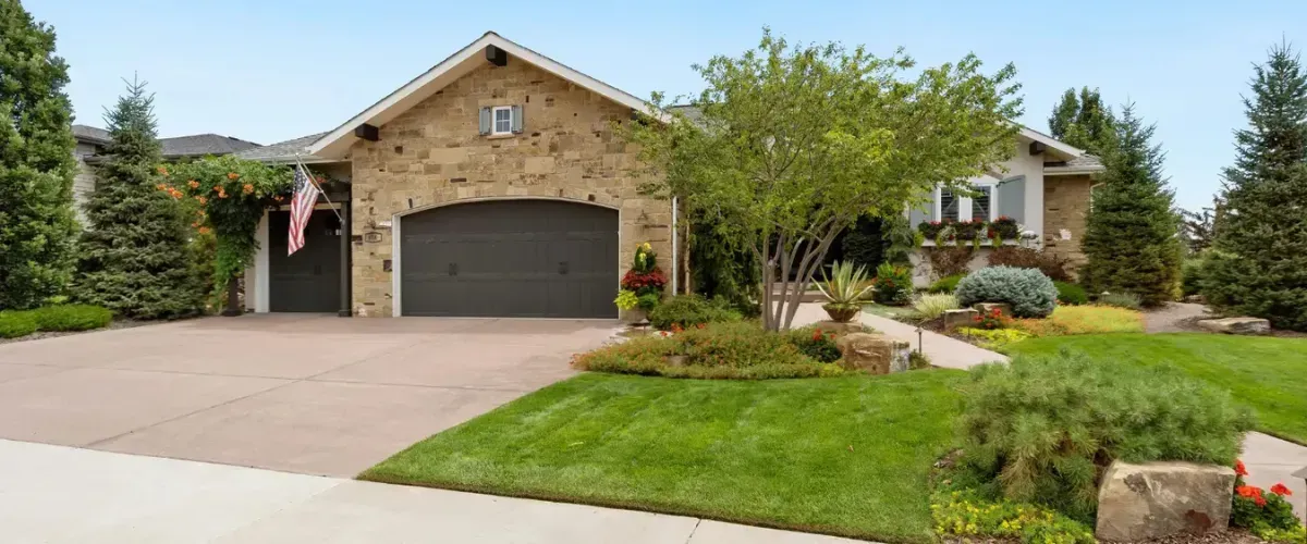 Charming stone house with a landscaped front yard, lush greenery, and a spacious driveway.