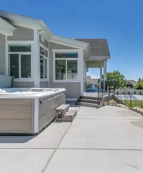 Modern home backyard with a hot tub, spacious concrete patio, and steps leading to a covered porch