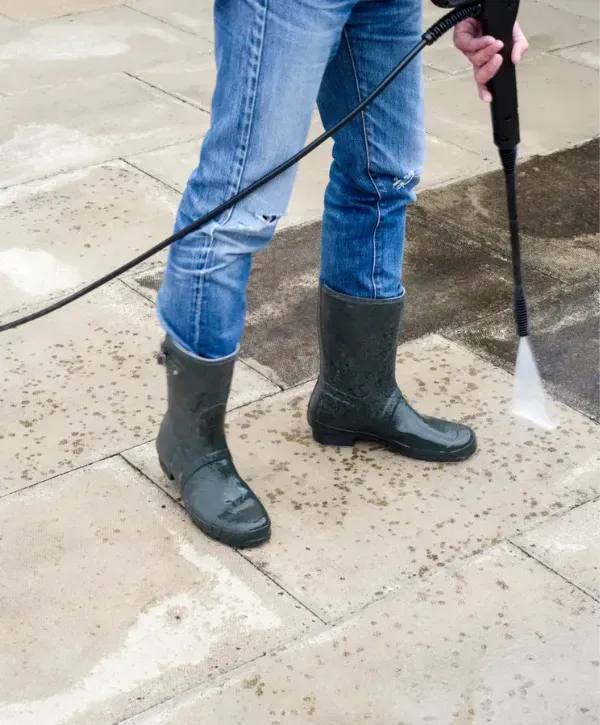 Close-up of a person pressure washing a driveway while wearing rubber boots.