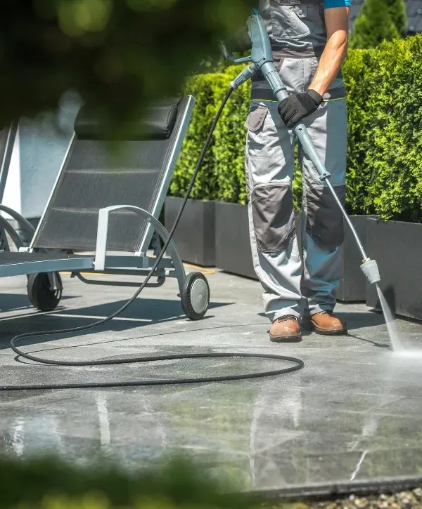 Worker cleaning an outdoor patio with a pressure washer to remove dirt and grime from the surface.