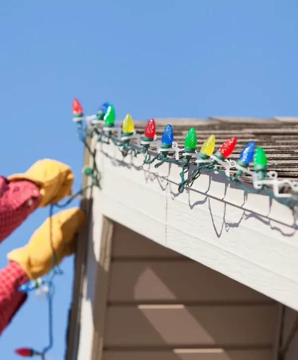 Worker installing colorful Christmas lights on a home in Plainfield, Indiana.