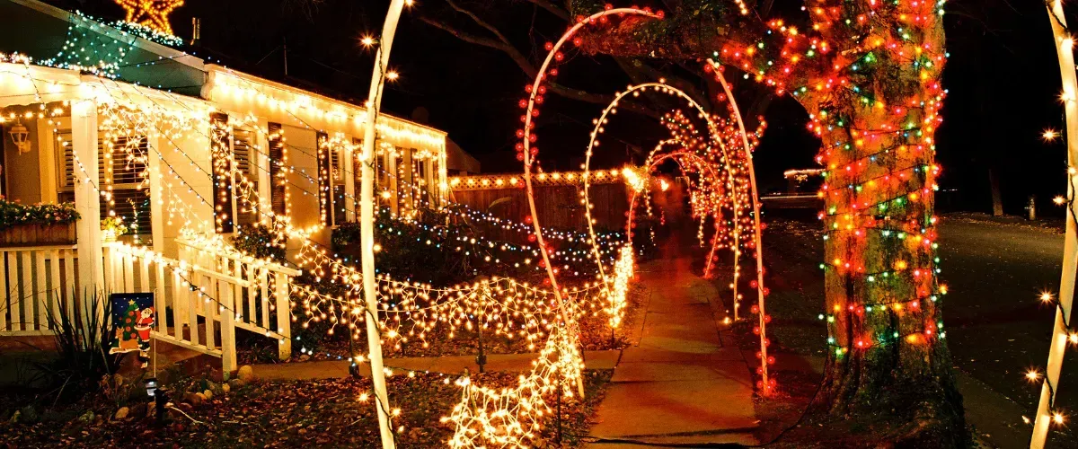 Neighborhood walkway covered with arches of bright Christmas lights and decorated trees.