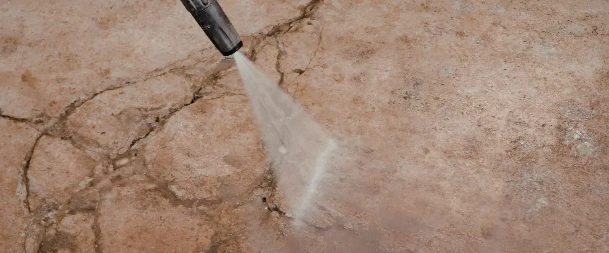 Pressure washer cleaning dirt from cracked concrete