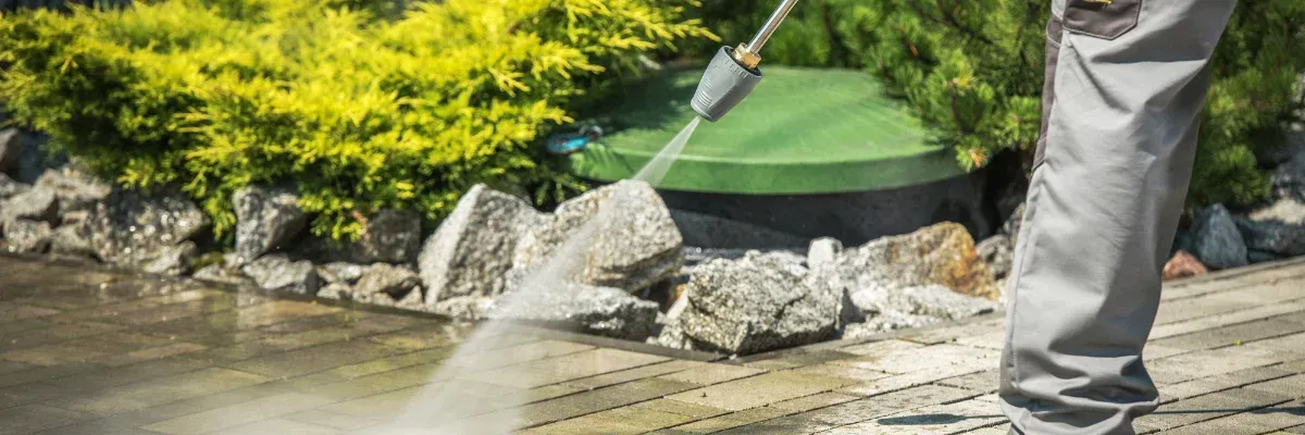 Person power washing concrete driveway outside modern home.