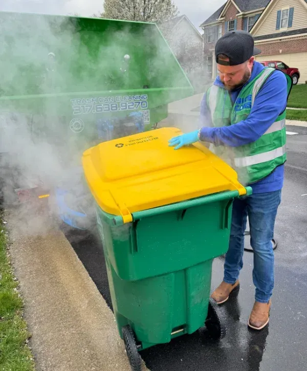 A man pressure washing a green trash can next to a 'Nice Cans' branded truck and cleaning trailer.