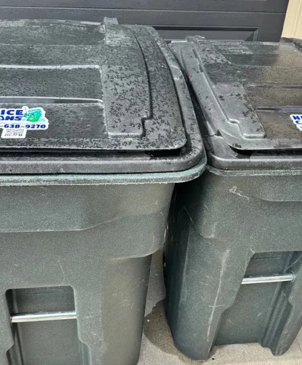 A close-up view of two dark green, wet trash cans with closed lids, showing water droplets on their surfaces.
