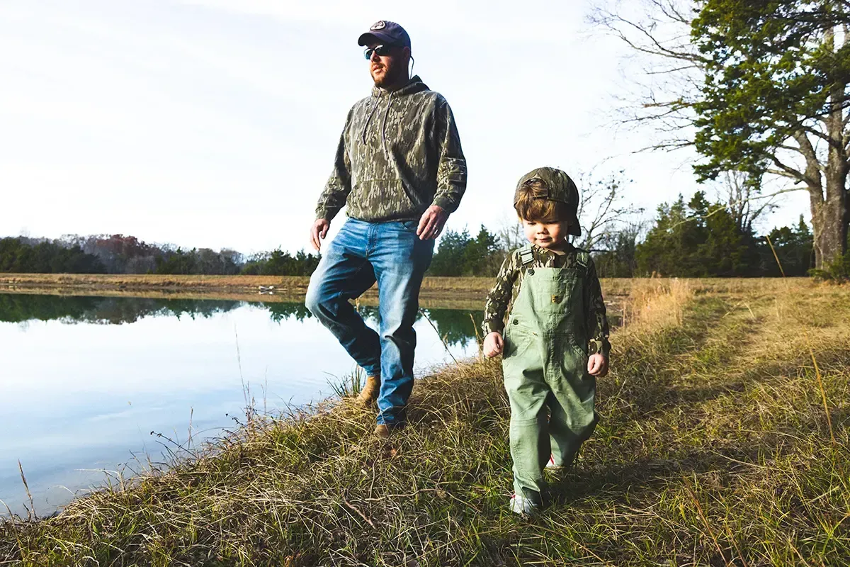 Father and child wearing outdoor adventure gear and camo clothing from top clothing brands amazon near a scenic lakeside