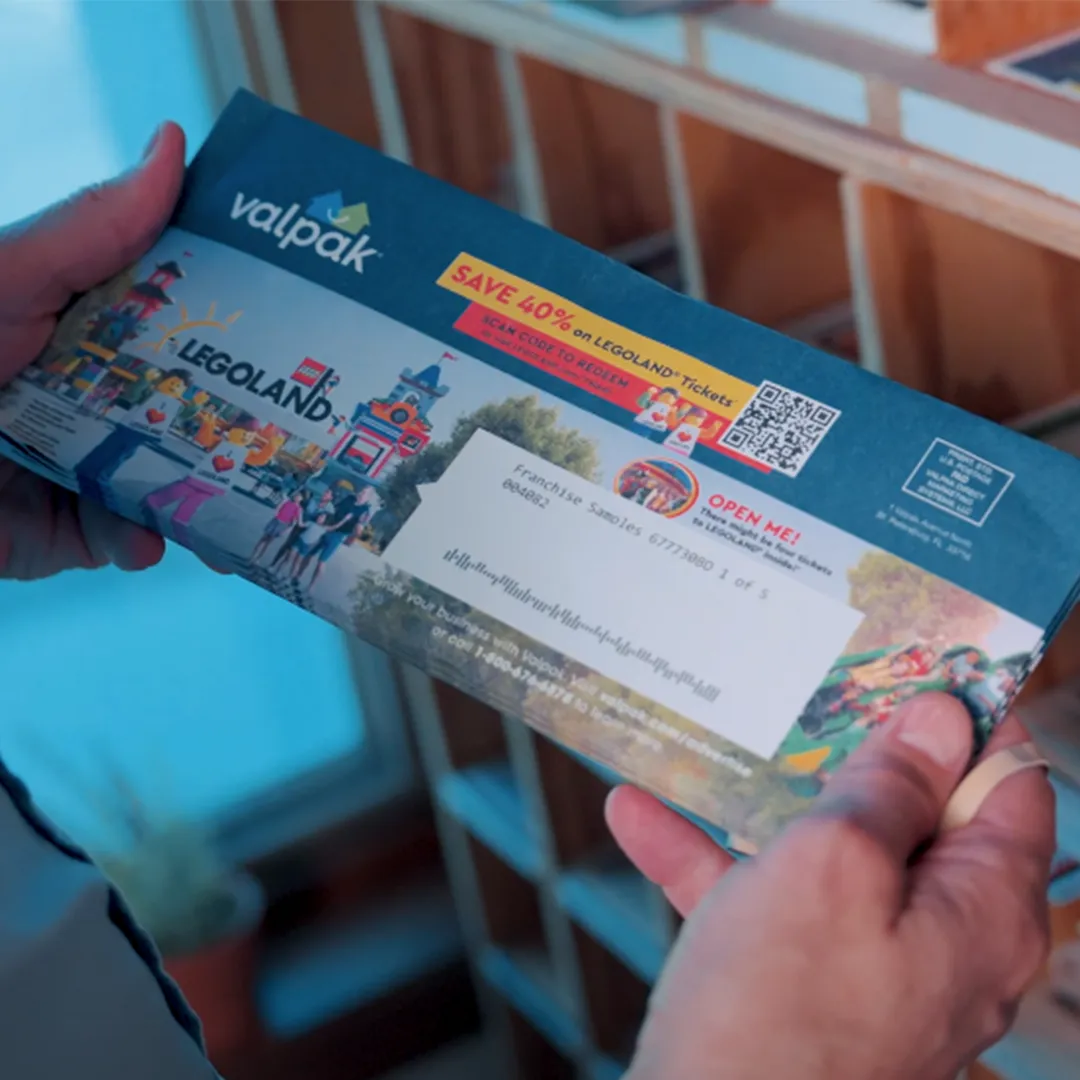 A man holding a Valpak envelope in front of shelves.