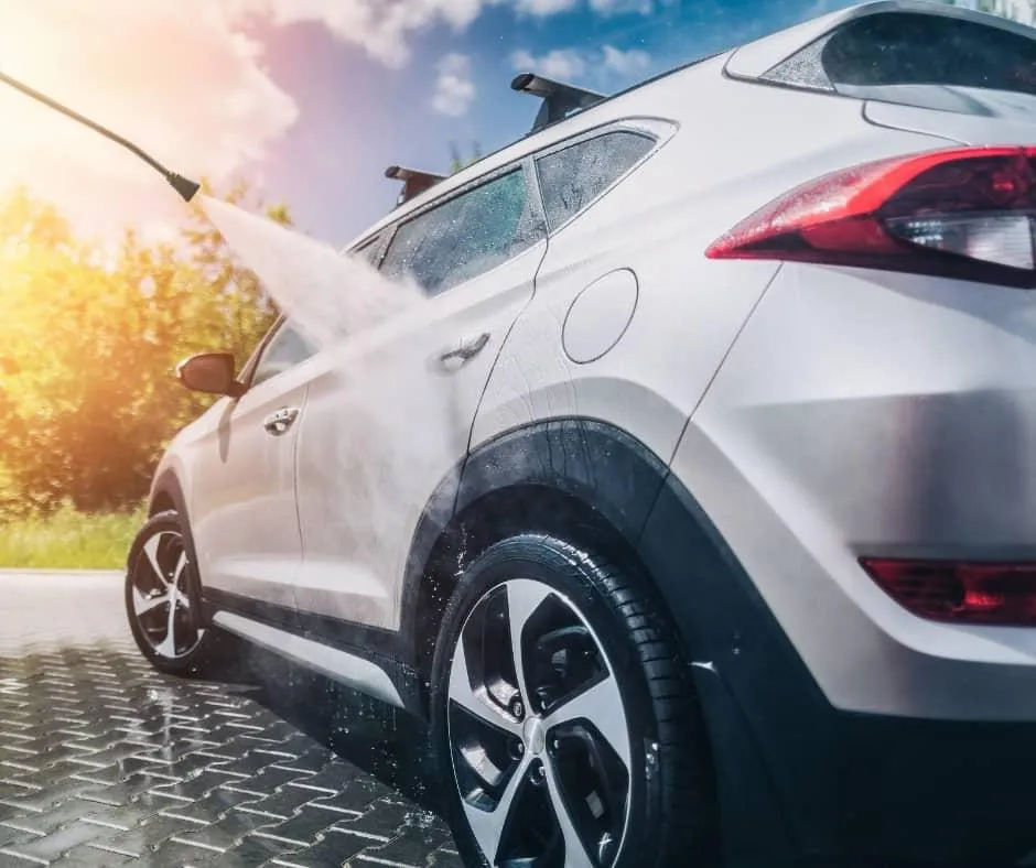 Exterior car wash service with a high-pressure water jet cleaning a white SUV on a bright sunny day in Bend, Oregon, emphasizing the vehicle's shine and the eco-friendly outdoor cleaning service.