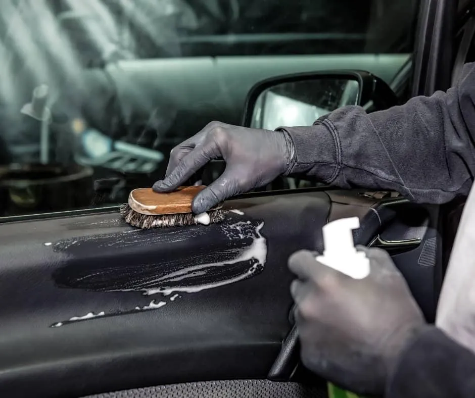 Close-up of a detailed interior car cleaning service in Bend, Oregon, with gloved hands using a premium brush and foam on a dashboard, showcasing meticulous auto care and maintenance.